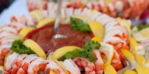A close-up of a shrimp cocktail platter garnished with lemon wedges and parsley, served with a dipping sauce.