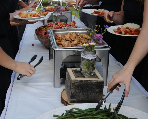 Guests serving themselves food from a catering buffet featuring chafing dishes and fresh salads.