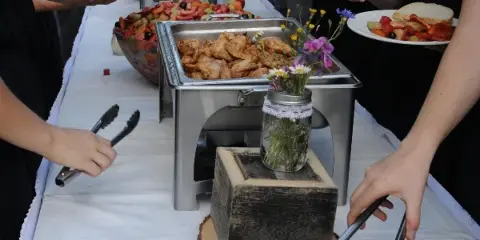 Guests serving themselves food from a catering buffet featuring chafing dishes and fresh salads.