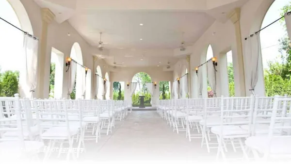 Interior view of an open-air wedding chapel with white chairs arranged in rows and arched columns.