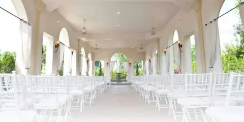 Interior view of an open-air wedding chapel with white chairs arranged in rows and arched columns.