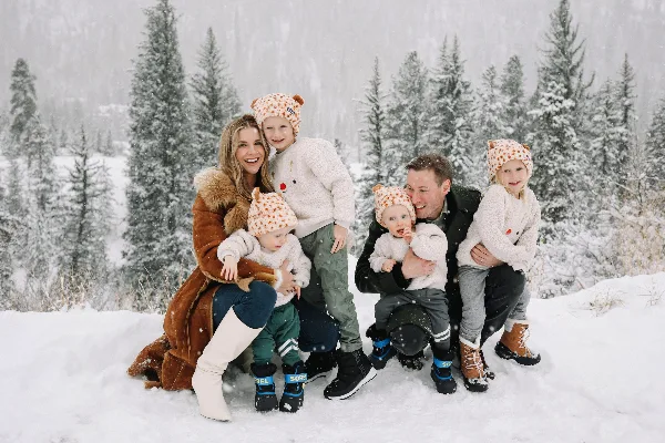 A family of six posing for a professional portrait in a snowy forest setting.