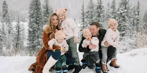 A family of six posing for a professional portrait in a snowy forest setting.