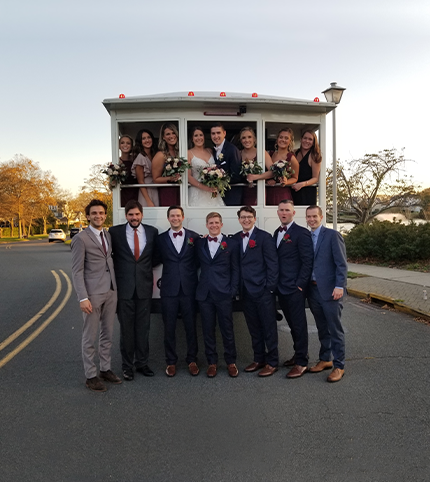 A wedding party posing in front of a white wedding trolley.
