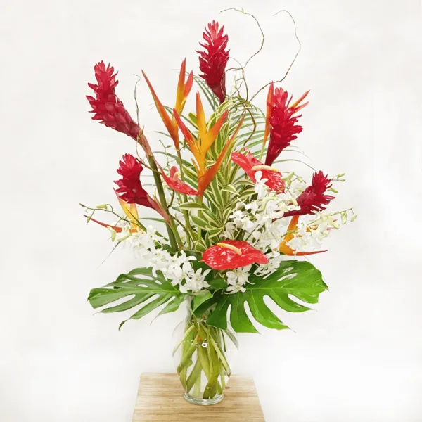 Large tropical floral arrangement with red heliconia, white orchids, and monstera leaves in a glass vase
