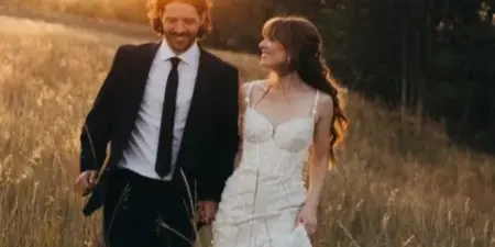 A bride and groom walking through a tall grass field during golden hour.