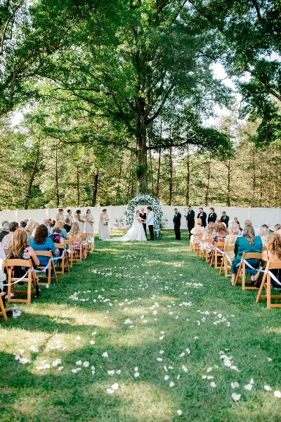 Outdoor wedding ceremony with a bride and groom at an altar surrounded by a wedding party and seated guests.