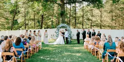 Outdoor wedding ceremony with a bride and groom at an altar surrounded by a wedding party and seated guests.