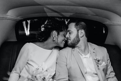 A bride and groom sharing a kiss in the back seat of a luxury car.