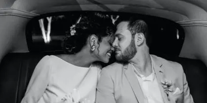 A bride and groom sharing a kiss in the back seat of a luxury car.