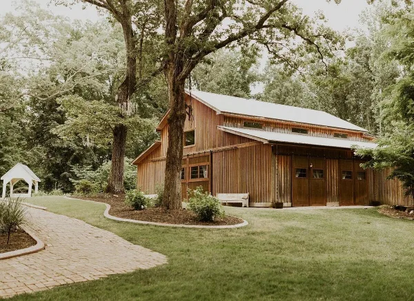 Exterior view of a wooden barn wedding venue with a paved walkway and manicured lawn.