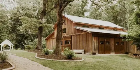 Exterior view of a wooden barn wedding venue with a paved walkway and manicured lawn.