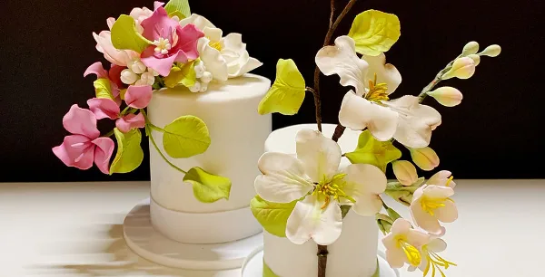 A white wedding cake decorated with elaborate pink and white sugar flowers and green leaves.
