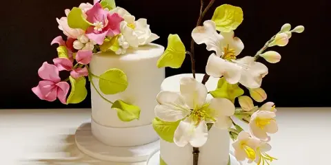 A white wedding cake decorated with elaborate pink and white sugar flowers and green leaves.