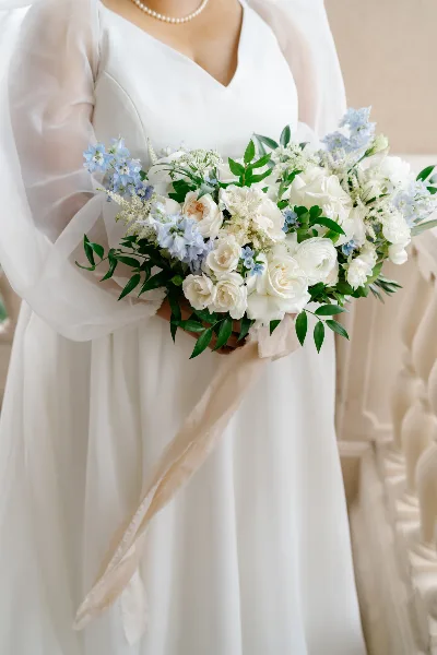 A close-up of a bride holding a large bouquet of white roses and blue flowers.