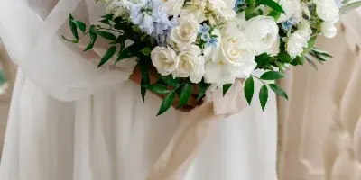 A close-up of a bride holding a large bouquet of white roses and blue flowers.