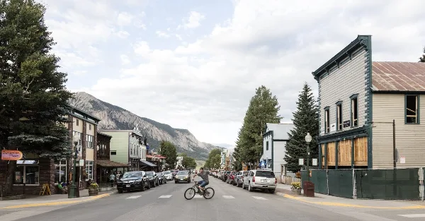 Street scene in Crested Butte with parked cars, storefronts, and a mountain in the background.