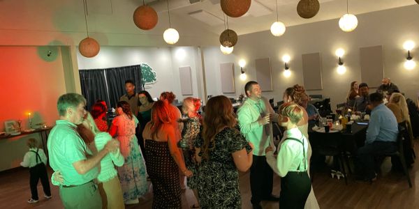 Guests dancing at a wedding reception with a DJ booth in the background.