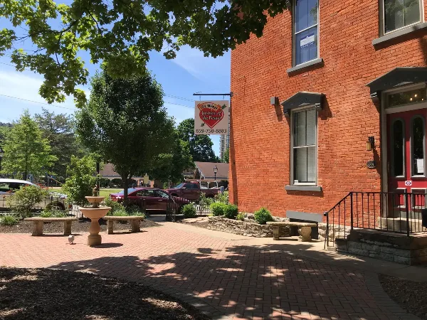 Exterior view of a red brick office building with a hanging sign for Steve Hoffman Justice of the Peace, featuring a courtyard with a fountain and brick paving.