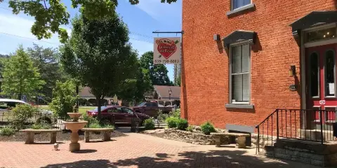Exterior view of a red brick office building with a hanging sign for Steve Hoffman Justice of the Peace, featuring a courtyard with a fountain and brick paving.