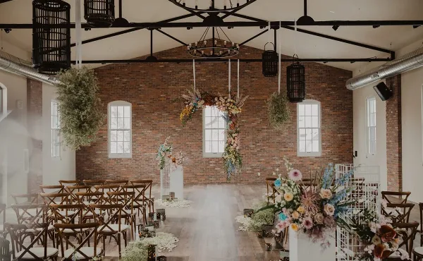 Interior view of a historic brick event venue set up for a wedding ceremony with wooden chairs and floral arrangements.