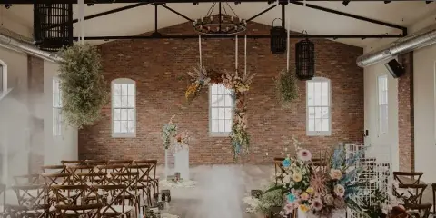 Interior view of a historic brick event venue set up for a wedding ceremony with wooden chairs and floral arrangements.