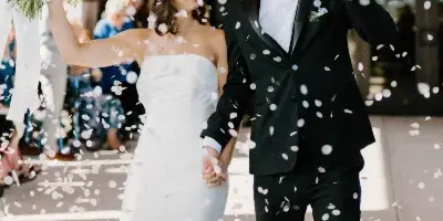 A bride and groom walking hand-in-hand while flower petals fall around them.