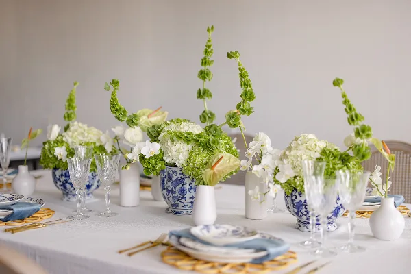 Elegant floral table arrangement featuring white hydrangeas, orchids, and greenery in blue and white ceramic vases.