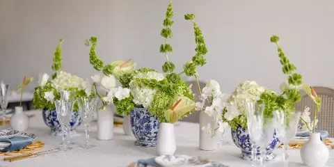 Elegant floral table arrangement featuring white hydrangeas, orchids, and greenery in blue and white ceramic vases.