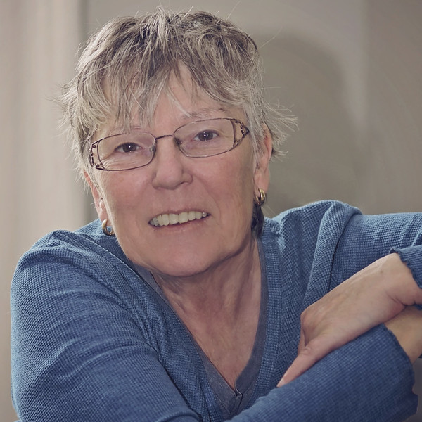 Portrait of a smiling woman with short blonde hair and glasses, wearing a blue top.