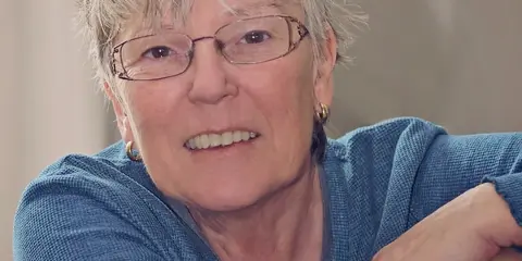 Portrait of a smiling woman with short blonde hair and glasses, wearing a blue top.