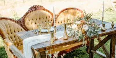 An outdoor wedding table setting with antique chairs, a wooden table, and floral centerpieces.