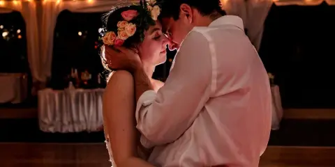 A bride wearing a floral crown and a groom in a white shirt share an intimate embrace during a wedding reception.