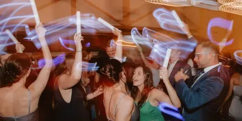 Guests dancing at a wedding reception with glow sticks and event lighting.