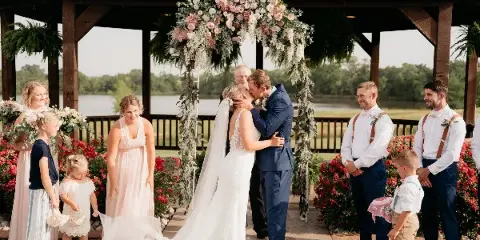 A bride and groom kissing during a wedding ceremony in a wooden gazebo with a lake view.