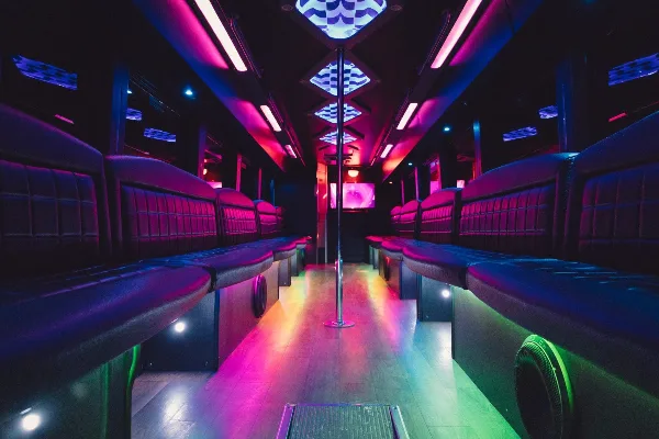 Interior of a party bus with leather bench seating, colorful LED lighting, and a center dance pole.