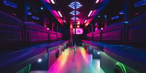 Interior of a party bus with leather bench seating, colorful LED lighting, and a center dance pole.