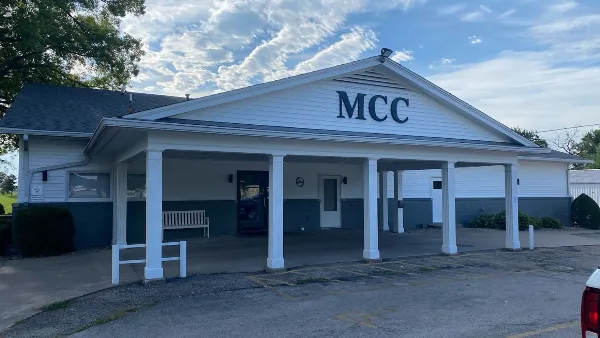 Exterior view of the Monmouth Country Club clubhouse featuring a white facade, covered porch with columns, and 'MCC' signage.