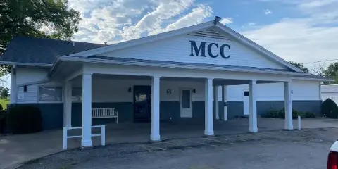 Exterior view of the Monmouth Country Club clubhouse featuring a white facade, covered porch with columns, and 'MCC' signage.