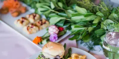A plated catering dish with macaroni and cheese, pulled pork, and a side salad on a table with floral arrangements.