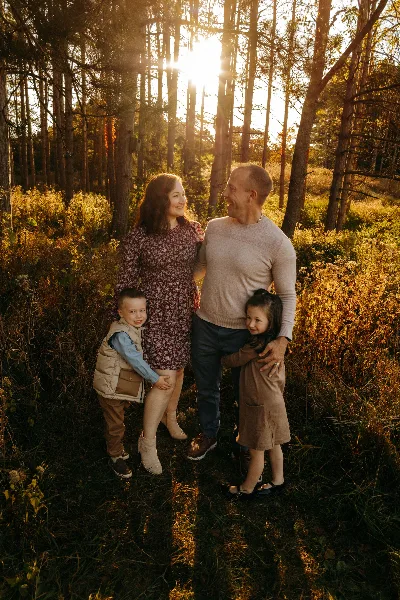 A family of four posing together in a sunlit forest during golden hour.