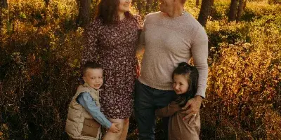 A family of four posing together in a sunlit forest during golden hour.