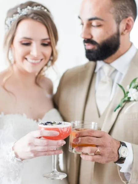 A bride and groom holding up cocktail glasses to toast during a wedding.