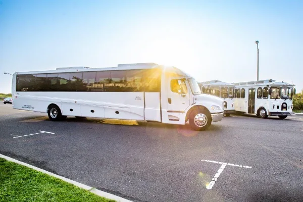 A fleet of white executive shuttles and trolleys parked in a lot at sunset.