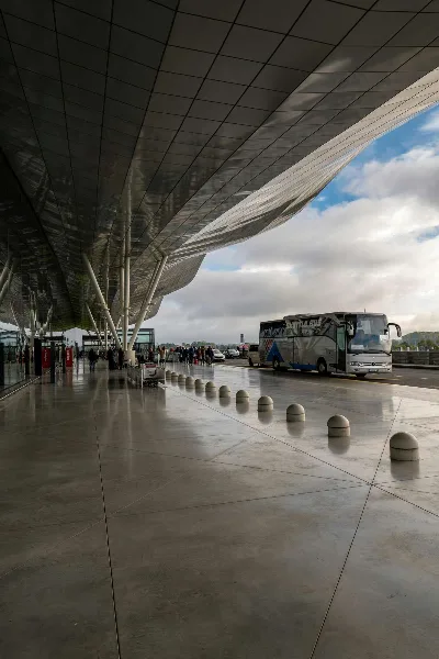 A charter bus parked at an airport terminal curb with passengers nearby.