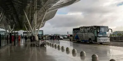 A charter bus parked at an airport terminal curb with passengers nearby.