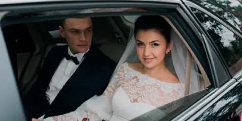 Bride and groom seated inside a luxury sedan during a wedding event