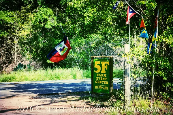 A green sign reading '5F Farm Event Center' stands by a road entrance, surrounded by lush greenery and international flags.