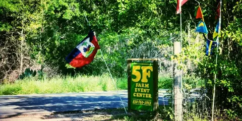 A green sign reading '5F Farm Event Center' stands by a road entrance, surrounded by lush greenery and international flags.