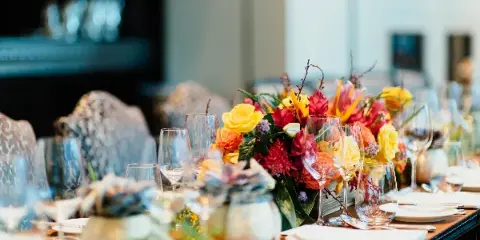 A close-up view of an elegant event table setting featuring a vibrant floral centerpiece with yellow and red flowers, glassware, and white plates.